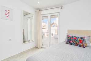 A bedroom with a bed, a large window, a sliding glass door, and a view of the outside.