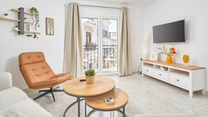 A modern living room with a leather chair, a wooden coffee table, a white TV stand, and a balcony with a view of buildings.