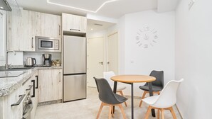 A modern kitchen with a microwave, refrigerator, and coffee maker. There is a dining area with a round table and two chairs.
