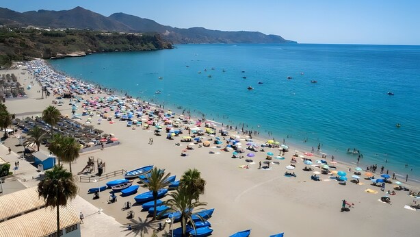 A beach with umbrellas, people, and boats.