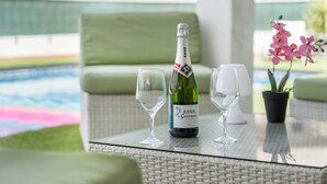 Una botella de vino Brut Anna De Coda di Modena, dos copas, una orquídea en maceta y una mesa de mimbre con vista a la piscina.