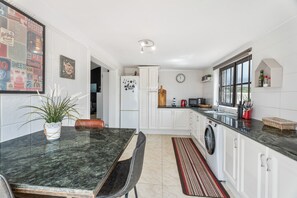 Une cuisine avec des meubles blancs, un plan de travail en granit, un lave-linge et un coin repas comprenant une table et des chaises.