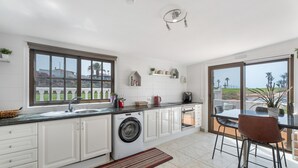 Cocina moderna con lavadora, zona de comedor con sillas y vistas al exterior.