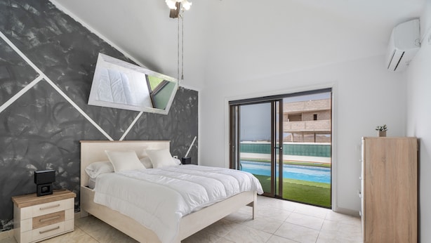 Un dormitorio con una cama, un televisor montado en la pared, una mesita de noche, un armario y vistas a una piscina a través de una puerta de cristal.