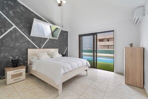 Une chambre avec un lit, un téléviseur fixé au mur, une table de chevet, une armoire et une vue sur une piscine, visible à travers une porte vitrée.