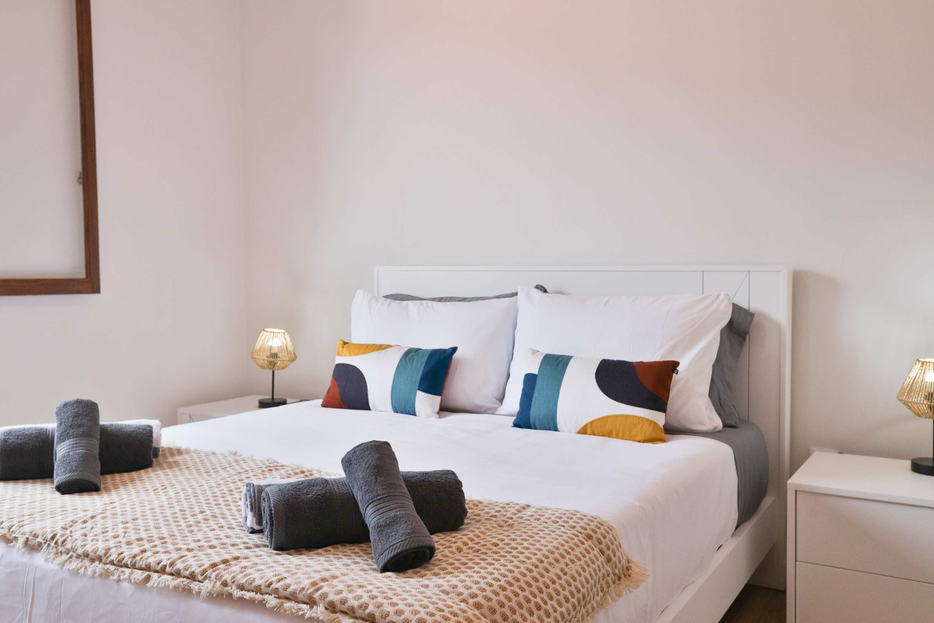 Un lit bien fait, avec une couverture à motifs, des coussins de différentes couleurs et deux lampes de chevet.