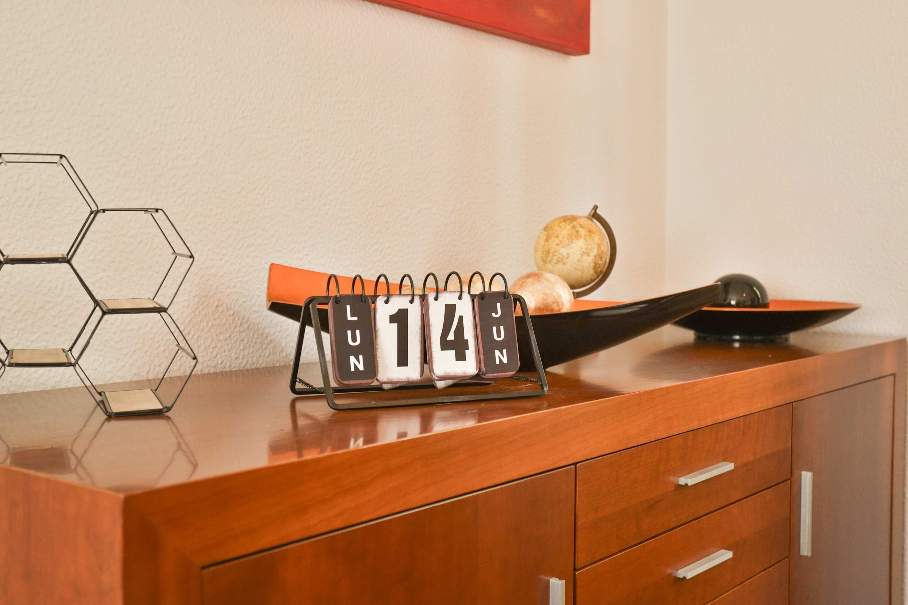 A wooden desk with a calendar displaying June 14, a bowl with a fruit, and a hexagonal metal sculpture.