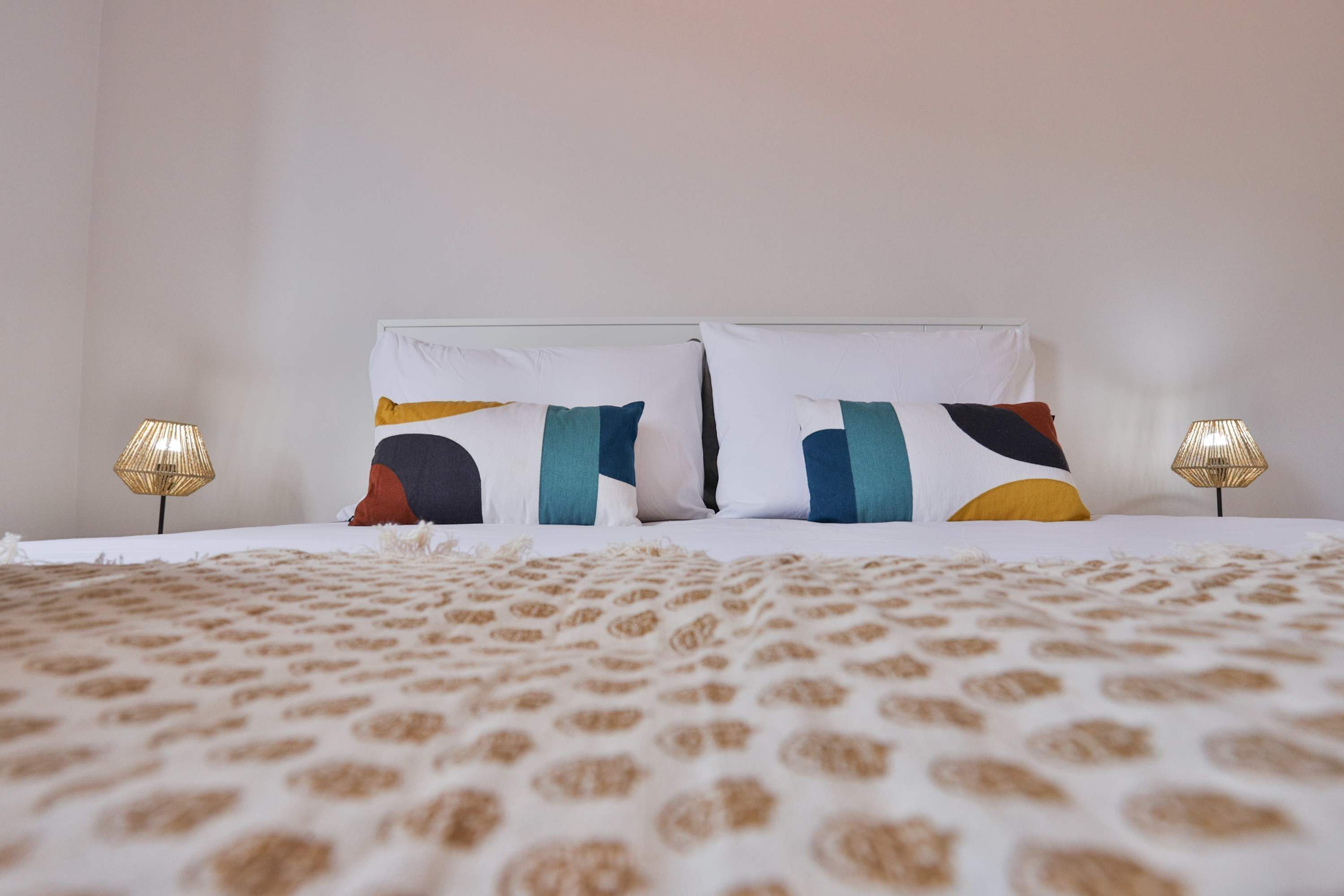 Un lit bien fait, avec une literie à motifs et deux coussins décoratifs.