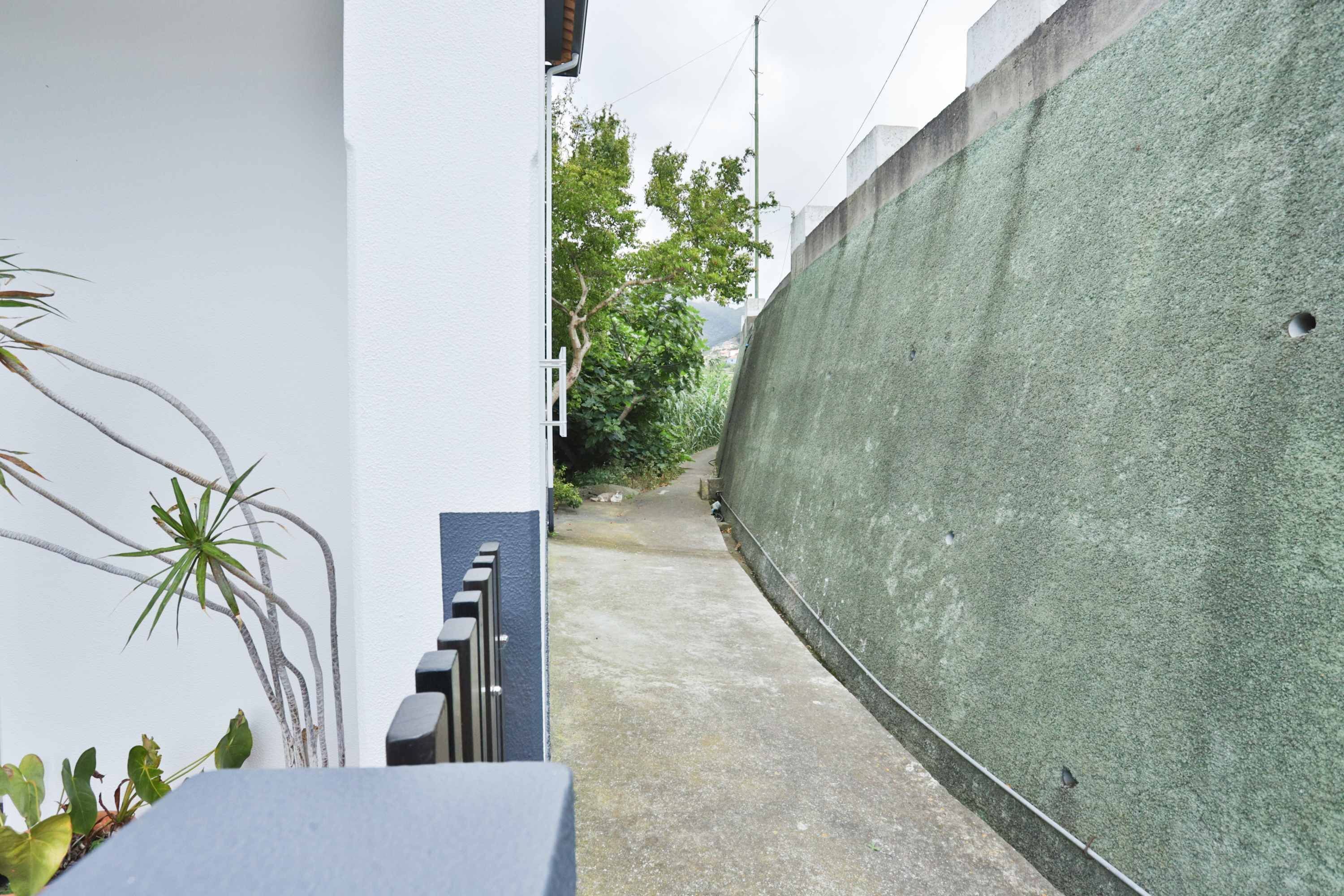 A narrow alleyway with a concrete wall on one side and a white building on the other.
