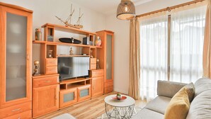 Una sala de estar moderna con muebles de madera, un televisor, una mesa redonda de centro y un ventanal con cortinas.