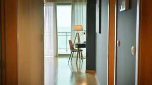 A hotel room with a wooden floor, a desk with a lamp, a chair, and a view of the sea through a window with curtains. - The Panoramic View in Machico (Machico)