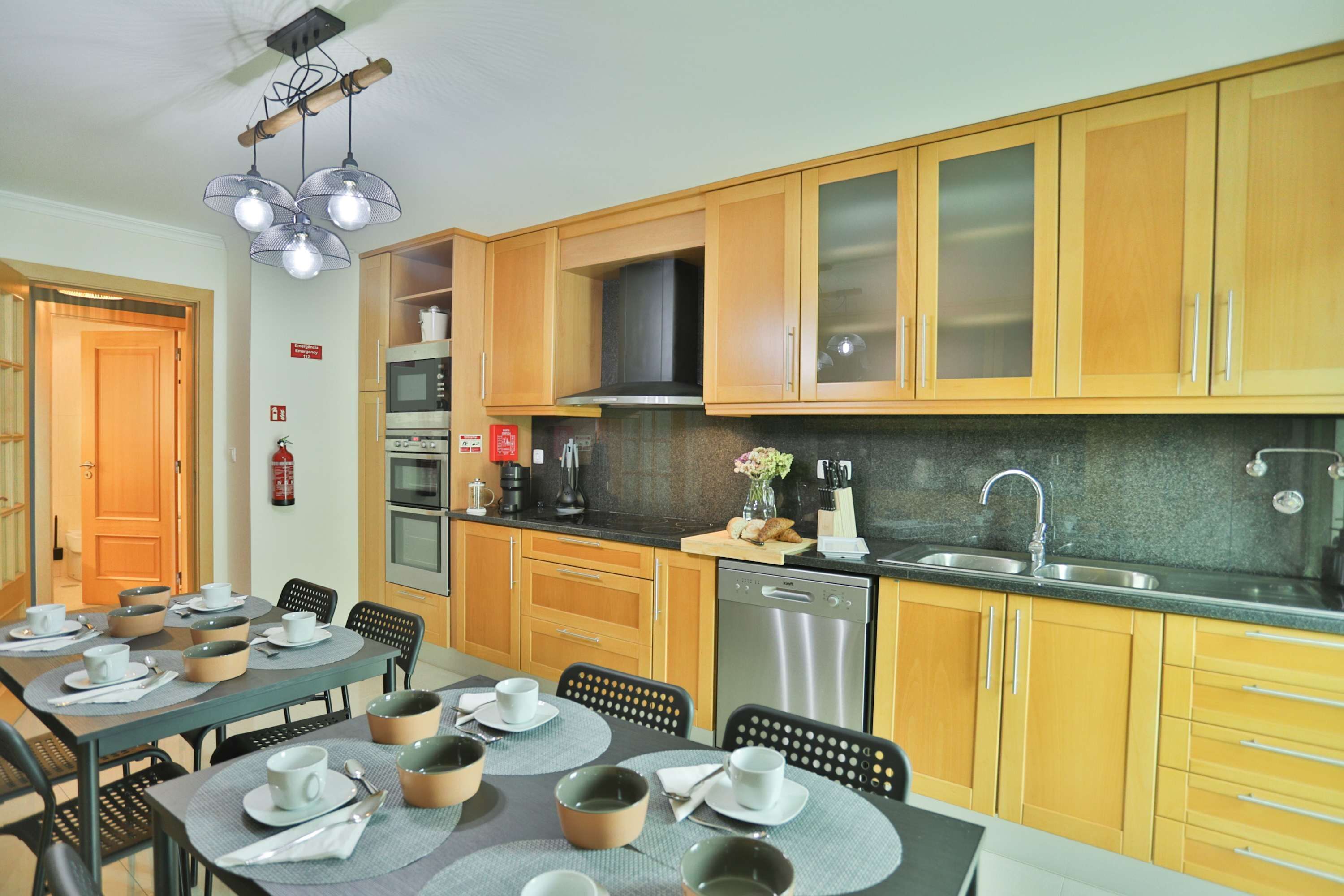 A modern kitchen with wooden cabinets, a stainless steel sink, and a dining area with a table set for four.