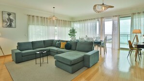 A modern living room with a sectional sofa, a small side table, and a dining area with a table and chairs. - The Panoramic View in Machico (Machico)