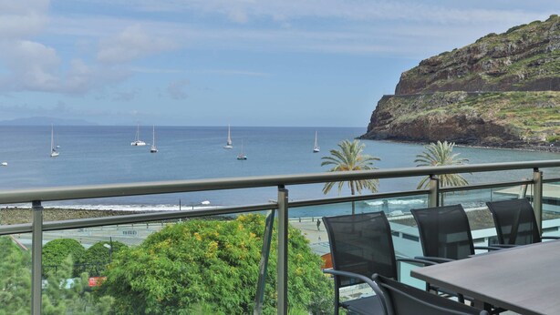A terrace with a view of the sea, featuring a table and chairs, and a rocky coastline with sparse vegetation. - The Panoramic View in Machico (Machico)