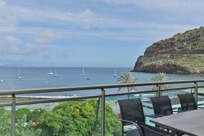 A terrace with a view of the sea, featuring a table and chairs, and a rocky coastline with sparse vegetation. - The Panoramic View in Machico (Machico)