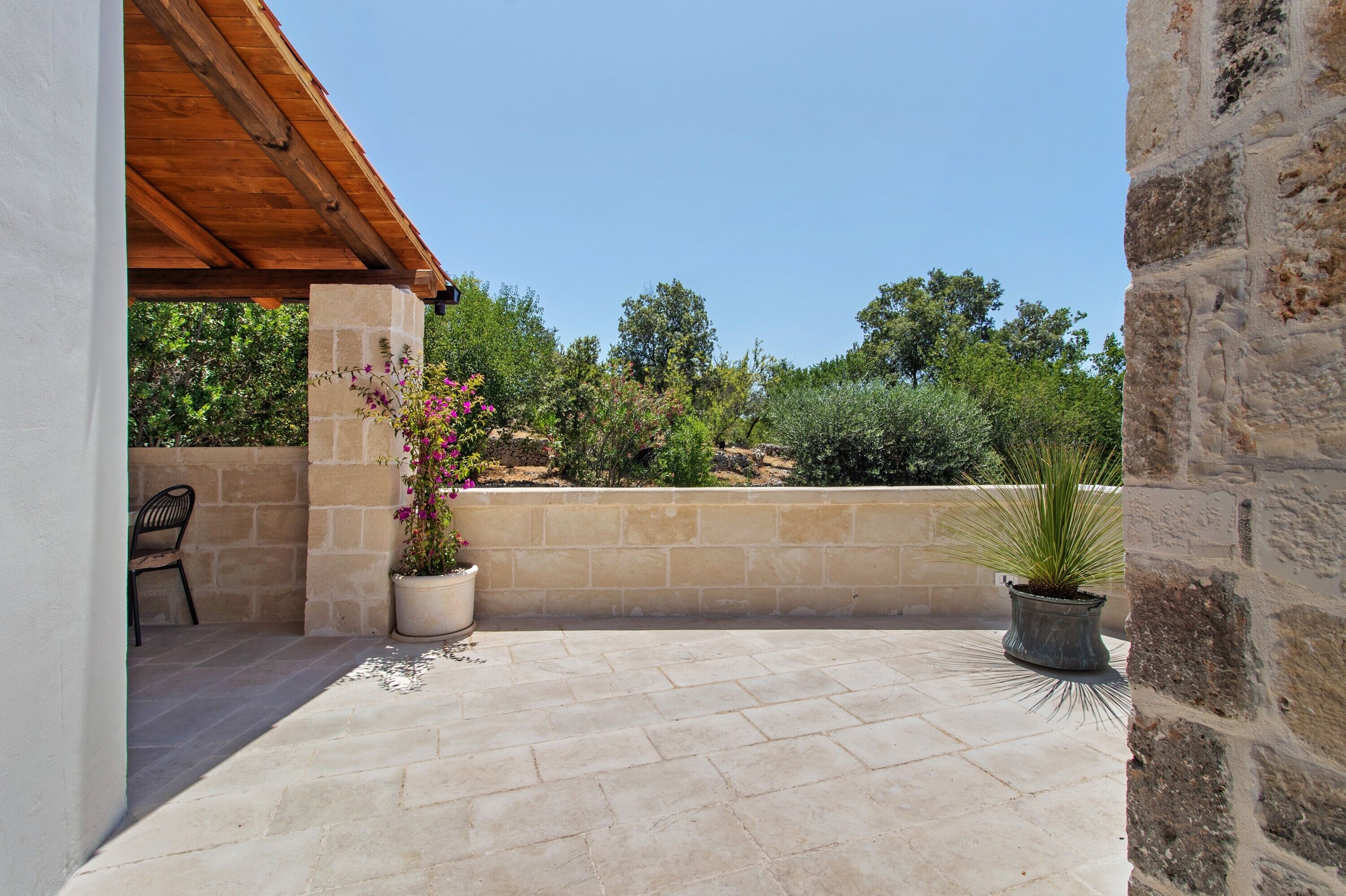 Un patio con piso de piedra, una pérgola de madera y plantas en macetas.