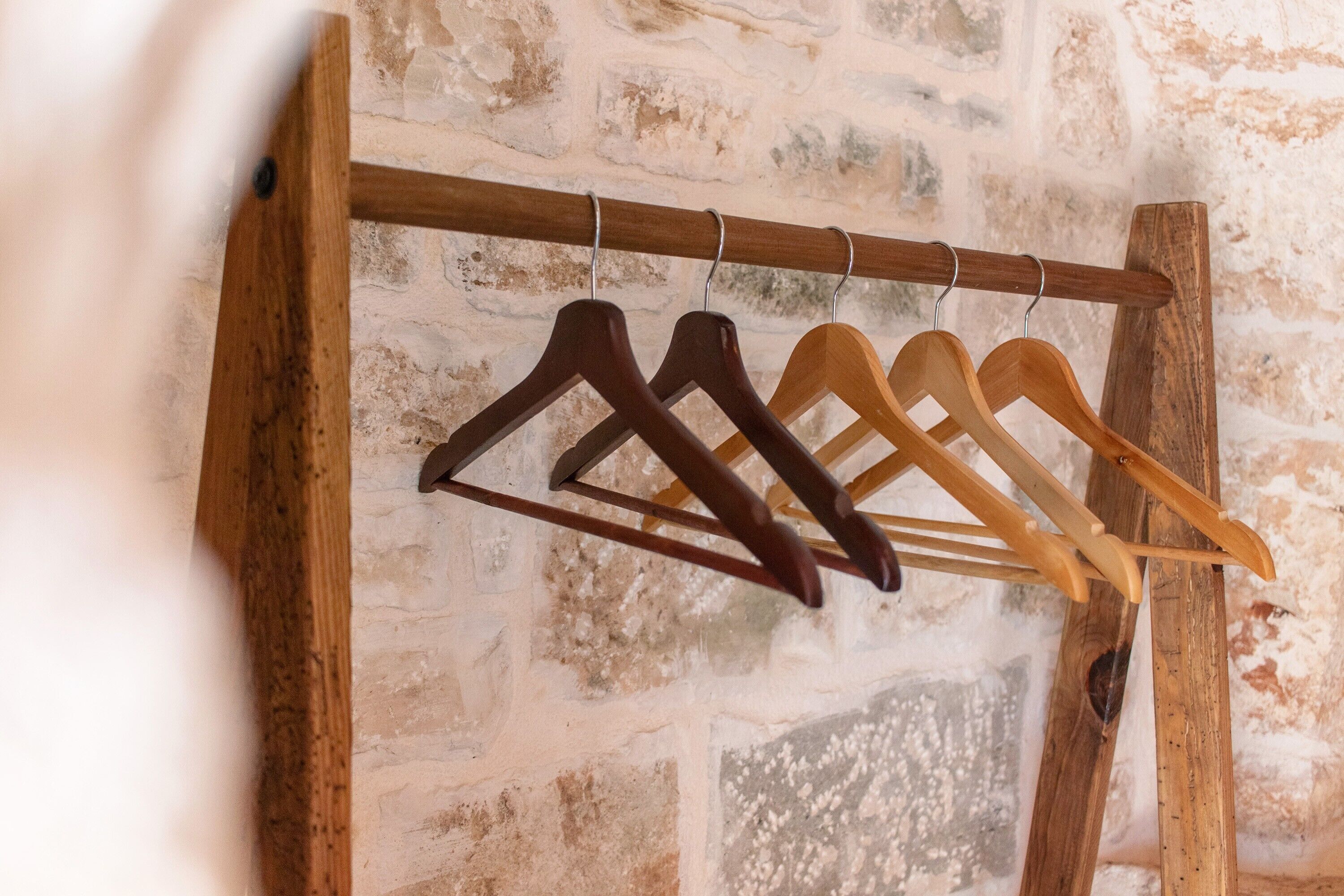 Un porte-vêtements en bois, muni de plusieurs cintres, est adossé à un mur en pierre à la texture particulière.