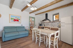 Une cuisine avec un réfrigérateur blanc, des poutres en bois, une table à manger avec des chaises, un canapé bleu et un tableau accroché au mur.