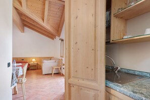Une cuisine en bois avec un évier, une table à manger avec des chaises et un petit coin salon comprenant une chaise et une lampe.