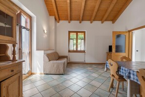 Une pièce avec un plafond en bois, une fenêtre avec des rideaux, un radiateur, une table avec des chaises et un meuble.