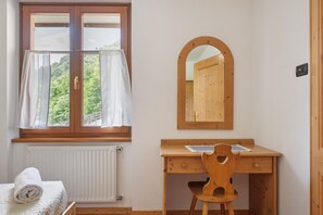 Une pièce avec un bureau en bois, une chaise, une fenêtre avec des rideaux, un radiateur et un miroir au mur.