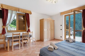 A bedroom with a bed, a wooden wardrobe, a dining table with chairs, and a window with curtains. - Room 'Stanza 3' with Mountain View, Private Terrace and Wi-Fi (Caldes)