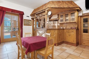 Une cuisine rustique avec des meubles en bois, une table à manger entourée de chaises et une fenêtre ornée de rideaux rouges.