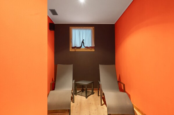 A room with two grey chairs, a small table, and a window with a curtain.