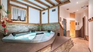 A spa area with a hot tub, stone wall, wooden beams, and a staircase leading to another room.