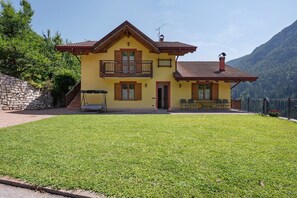 Une maison jaune à deux étages, dotée d’un balcon, d’un mur en pierre et d’une pelouse bien entretenue.
