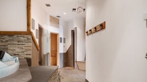 A hallway with a stone wall, a wooden staircase, and a clock on the wall.