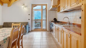 A kitchen with wooden cabinets, a dining table with chairs, a window with curtains, and a view of the outdoors.
