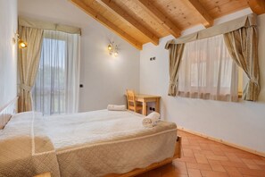 Une chambre avec un grand lit, des poutres apparentes en bois au plafond, un petit bureau et des rideaux.