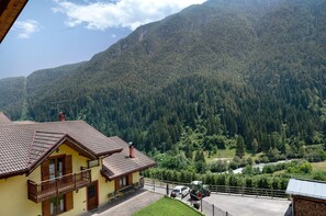 Un bâtiment jaune doté d’un balcon, une maison à toit rouge et un paysage montagneux en arrière-plan.