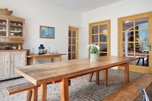 Une table à manger en bois avec des bancs, un meuble avec des portes en verre et un tableau encadré au mur.