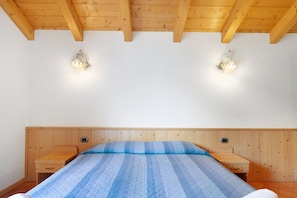 Une chambre à coucher avec une tête de lit en bois, un lit recouvert d’une couette bleue, deux tables de chevet et des lampes fixées au mur.