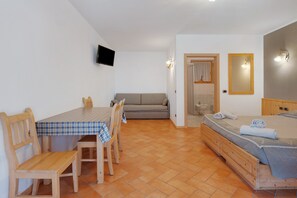 Une pièce comprenant une table à manger, des chaises, un canapé, un lit, une télévision et un miroir.