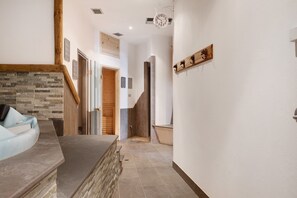 A hallway with a stone wall, a wooden staircase, and a clock on the wall.