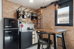 A kitchen with a refrigerator, stove, and hanging pots. There is a table with chairs and a hanging light bulb.