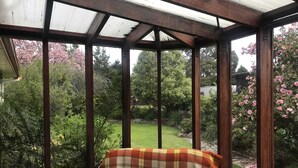 A conservatory with a wooden bench and a view of a garden. - Where comfort meets the mountains—close to everything,spacious,and pet-friendly! (Cromwell)