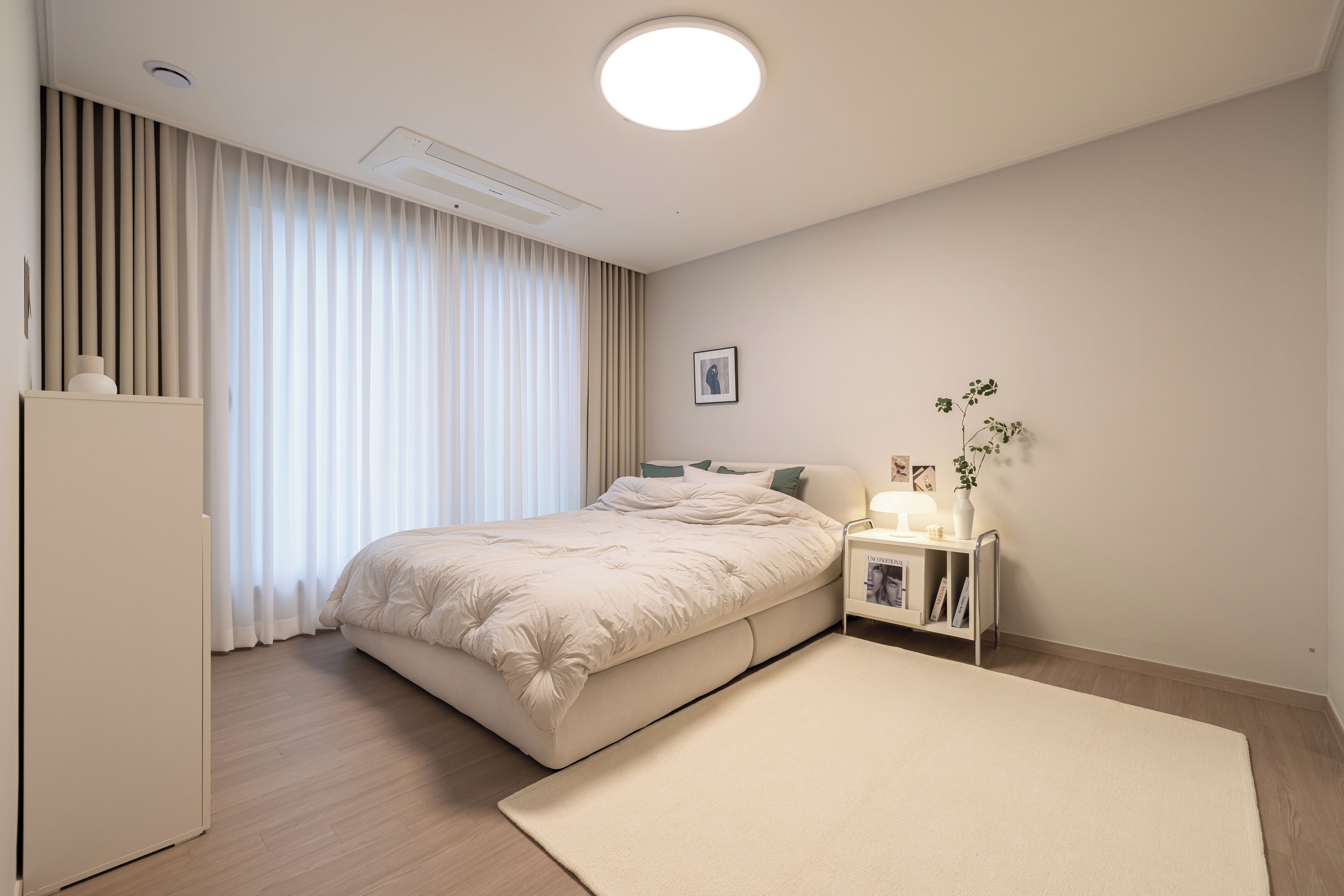 A modern bedroom with a large bed, a bedside table with a lamp, a small plant, and a picture on the wall.