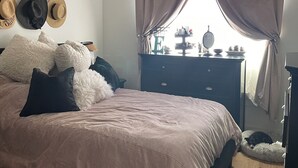 A bedroom with a bed, a ceiling fan, a dresser, and a window with curtains.