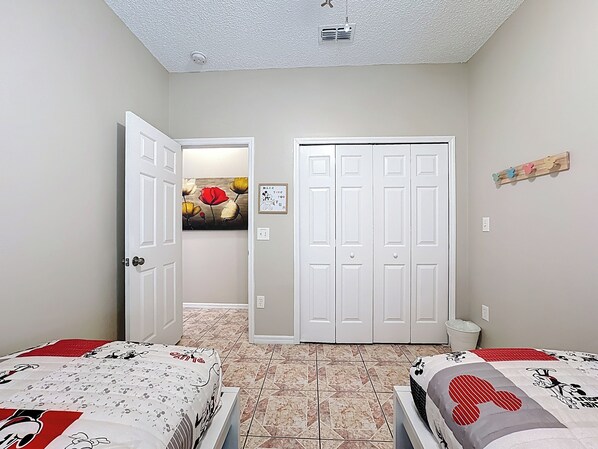 Un dormitorio con dos camas, una puerta que da a otra habitación, una lámpara fijada a la pared y un pequeño cubo de basura.