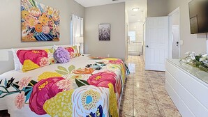 Un dormitorio con cama, ventilador de techo, televisión y un baño visible al fondo.