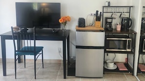 Eine kleine Küche mit Kühlschrank, Mikrowelle, Toaster und einem Esstisch mit einem Stuhl.