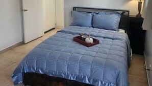 Ein Schlafzimmer mit Bett, Nachttisch, Lampe und einer Tür.