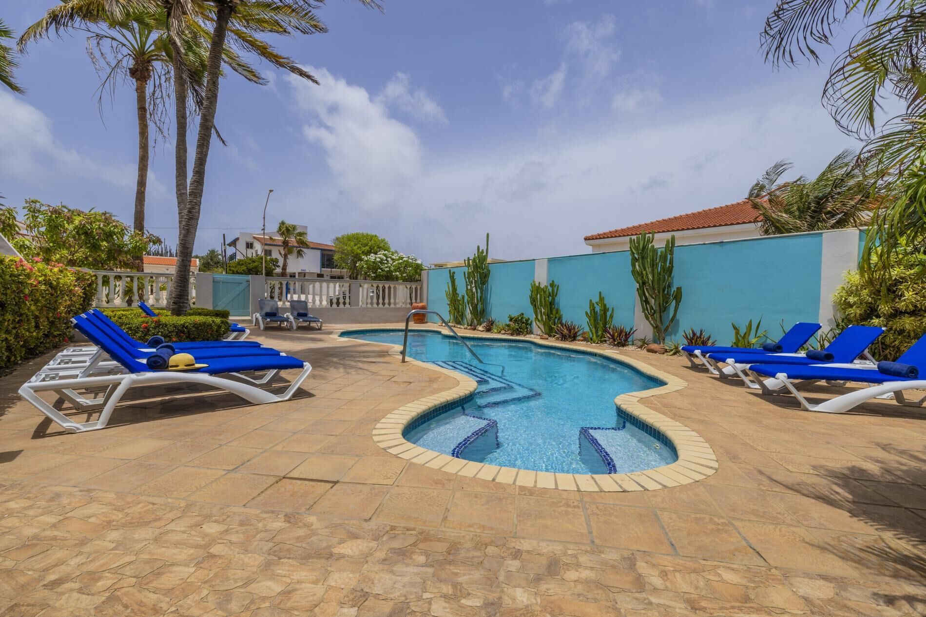 Ein Schwimmbad mit blauen Liegestühlen, Palmen und einer gefliesten Terrasse.