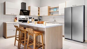A modern kitchen with a central island, wooden bar stools, stainless steel appliances, and white cabinetry.