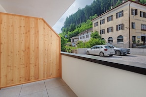A modern building with a wooden facade, a car parked on the street, and a view of a hillside with buildings.