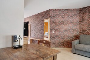 Une pièce avec un mur en briques, une table en bois, un canapé gris et un téléviseur.